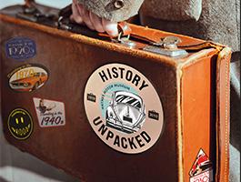 Man carrying suitcase with trail logo on "History Unpacked"
